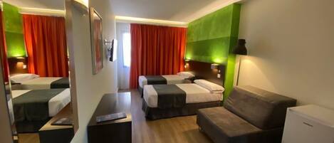 A hotel room with two beds, a sofa, a desk, and a small refrigerator.