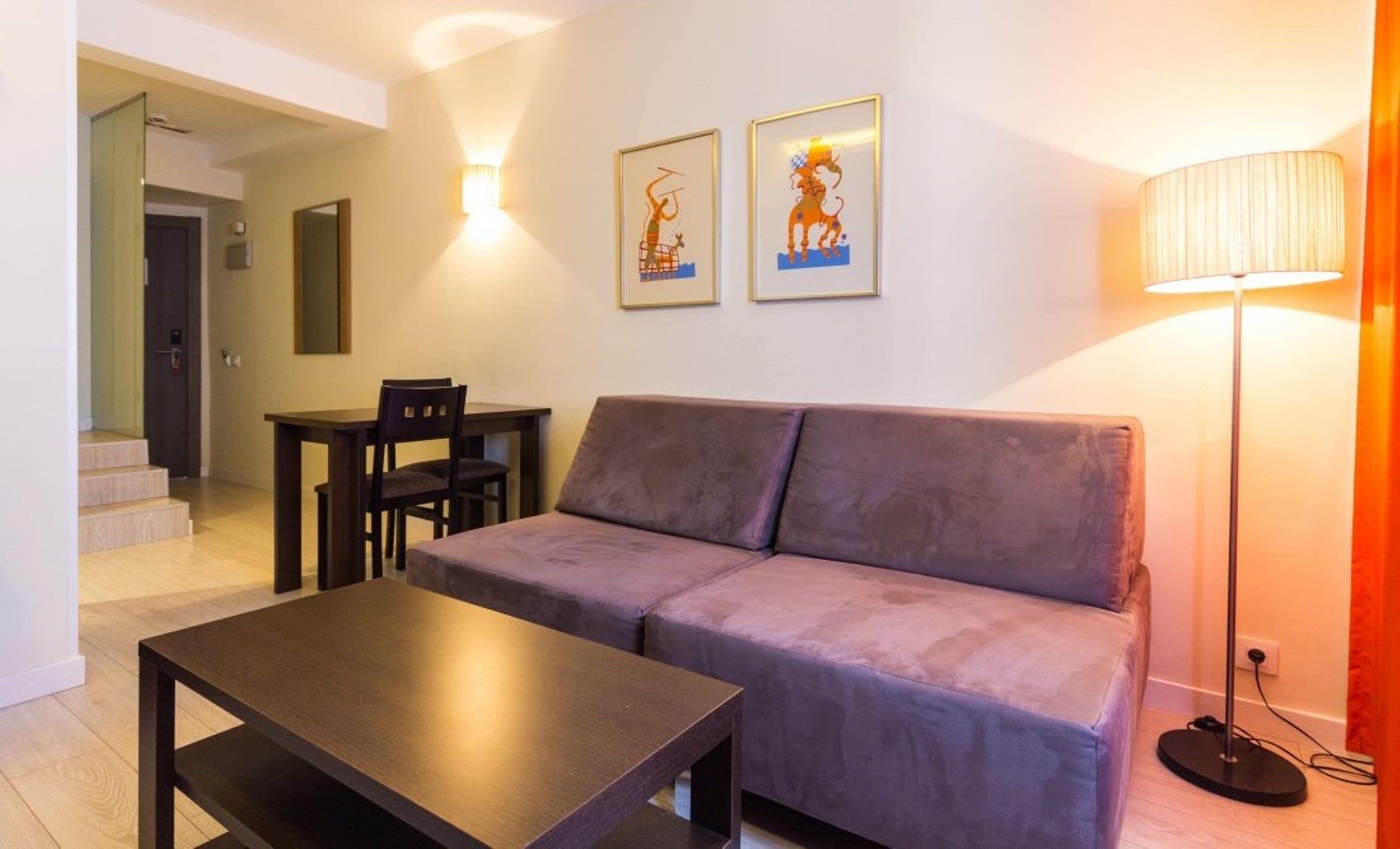 Ein Wohnzimmer mit einer Couch, einem Couchtisch, einem Esstisch mit Stühlen und zwei gerahmten Bildern an der Wand.