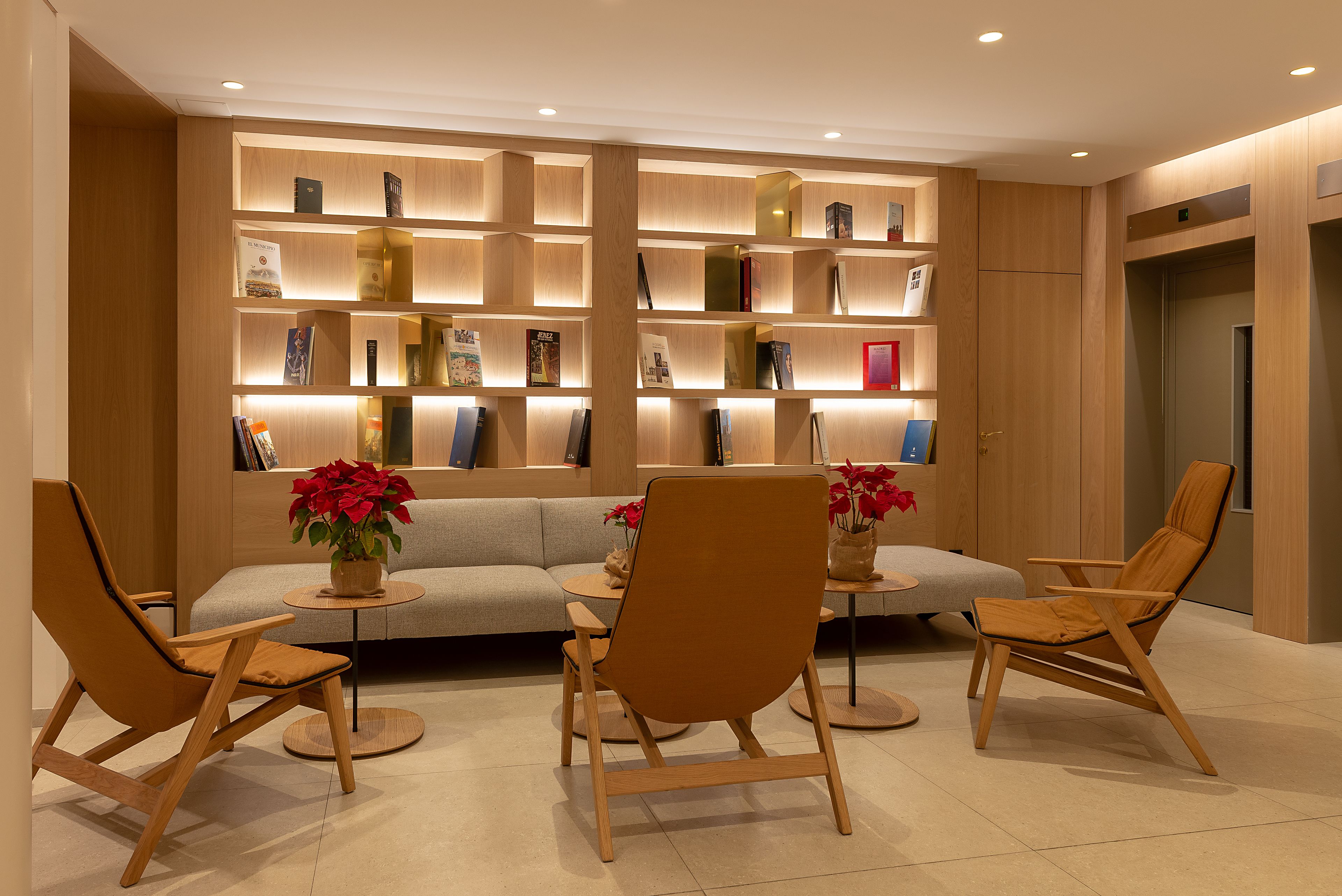 A modern interior with a sofa, three wooden chairs, a bookshelf, and a small table with a vase of flowers.