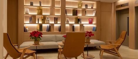 A modern interior with a sofa, three wooden chairs, a bookshelf, and a small table with a vase of flowers.