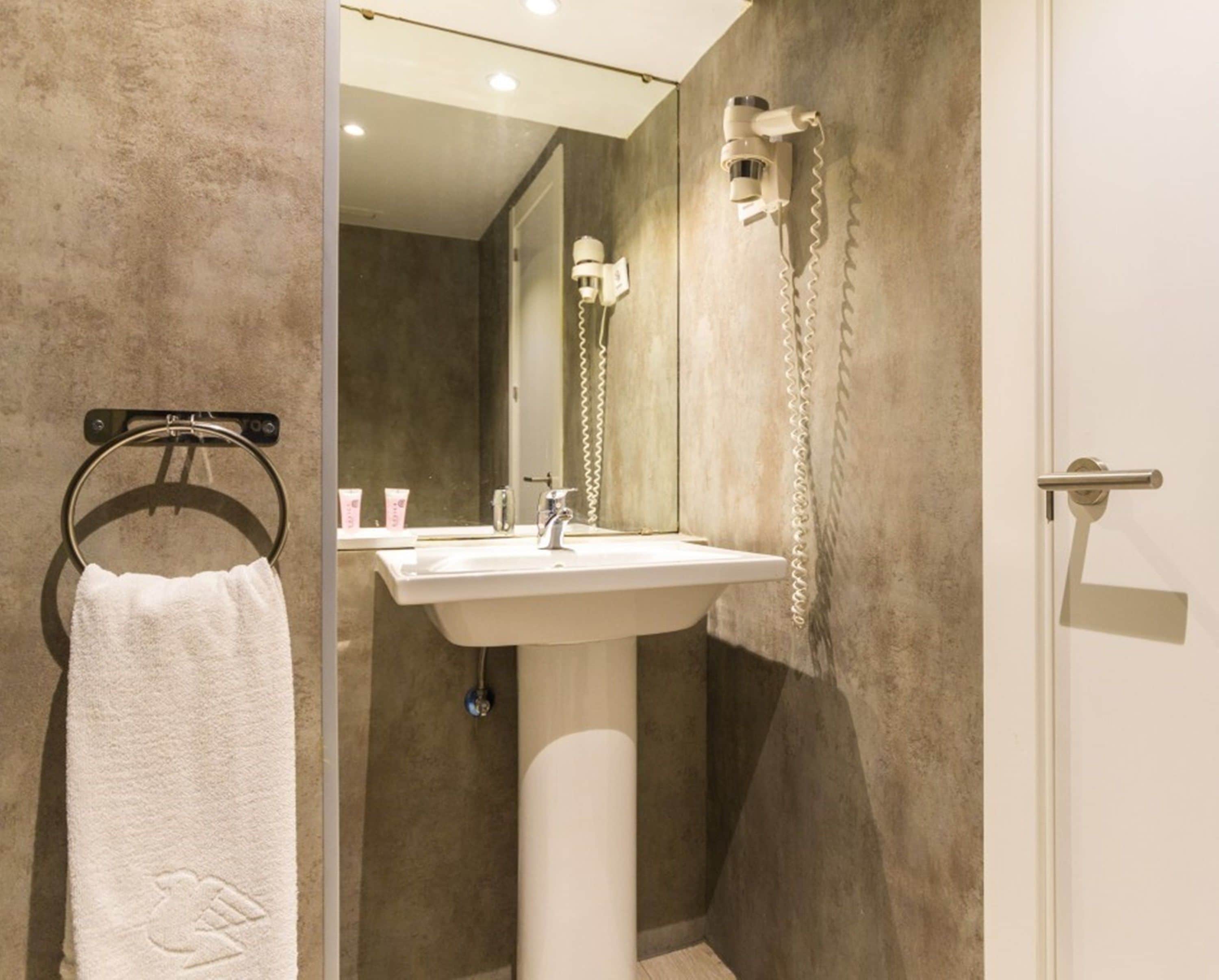 A modern bathroom with a white sink, a towel rack with a white towel, a mirror, and a shower with a wall-mounted showerhead.