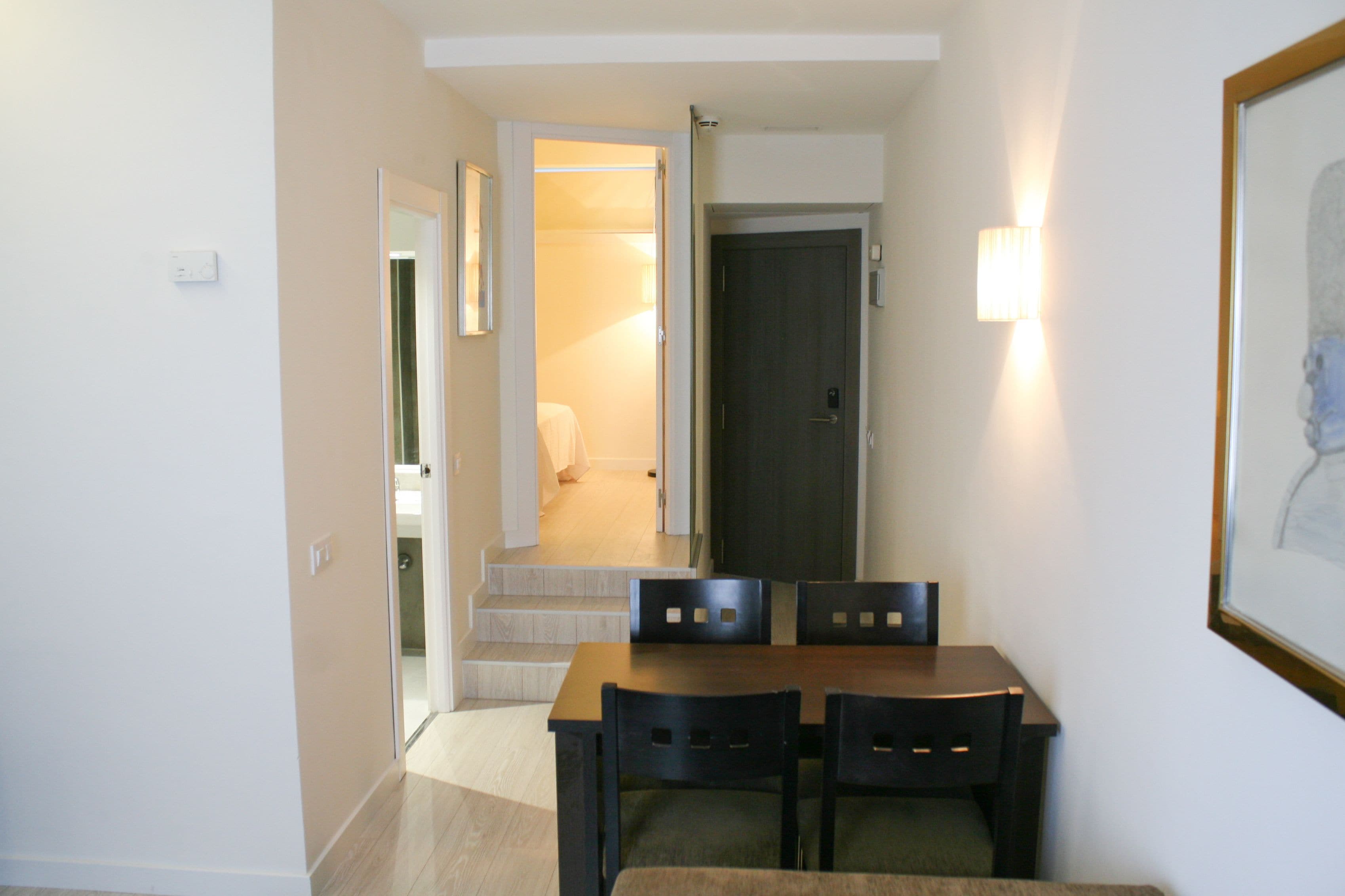 A dining area with a table and chairs, a door leading to another room, and a wall-mounted light fixture.