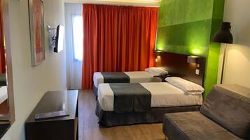 A hotel room with two beds, a sofa, a desk, and a green accent wall.