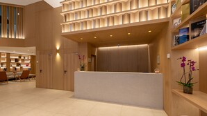 A modern reception area with a wooden reception desk, a seating area with chairs, and a bookshelf with books. - Apartamentos Recoletos (Madrid)