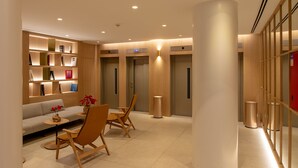 A modern lobby with a sofa, chairs, a bookshelf, and a reception desk. - Apartamentos Recoletos (Madrid)