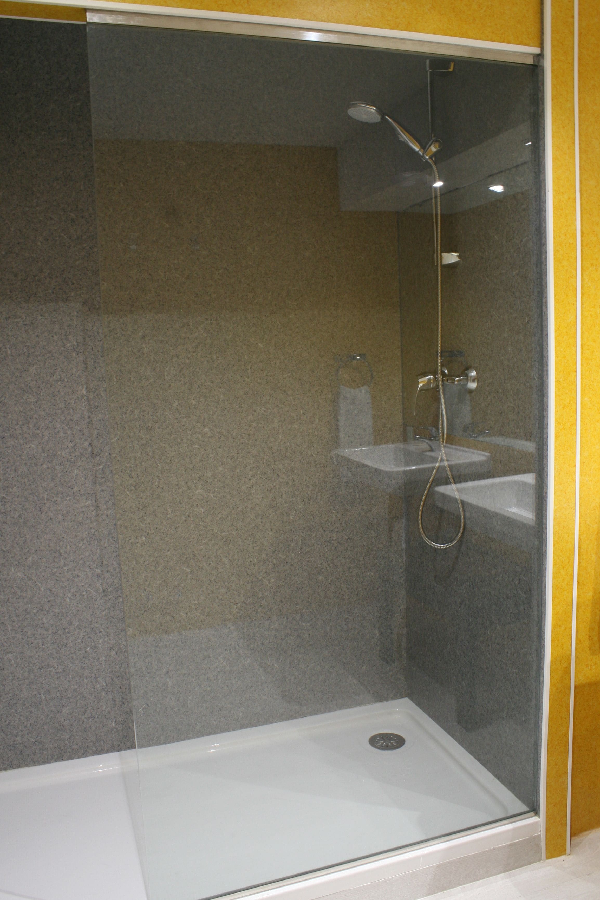 Een douchecel met glazen wanden, een wit wastafelmeubel en een handdouche.