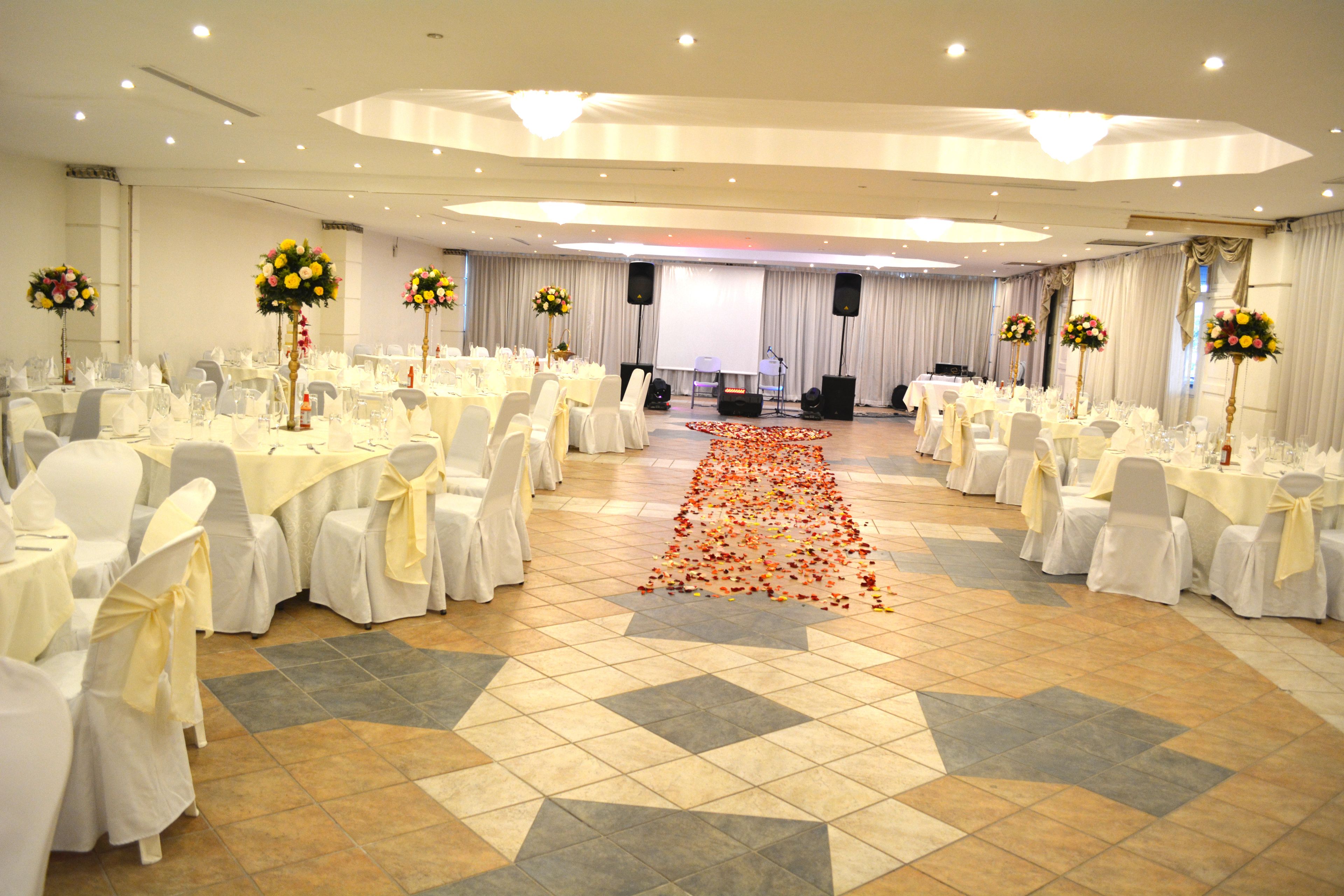 A banquet hall with rows of tables and chairs, a carpeted aisle, and floral centerpieces.