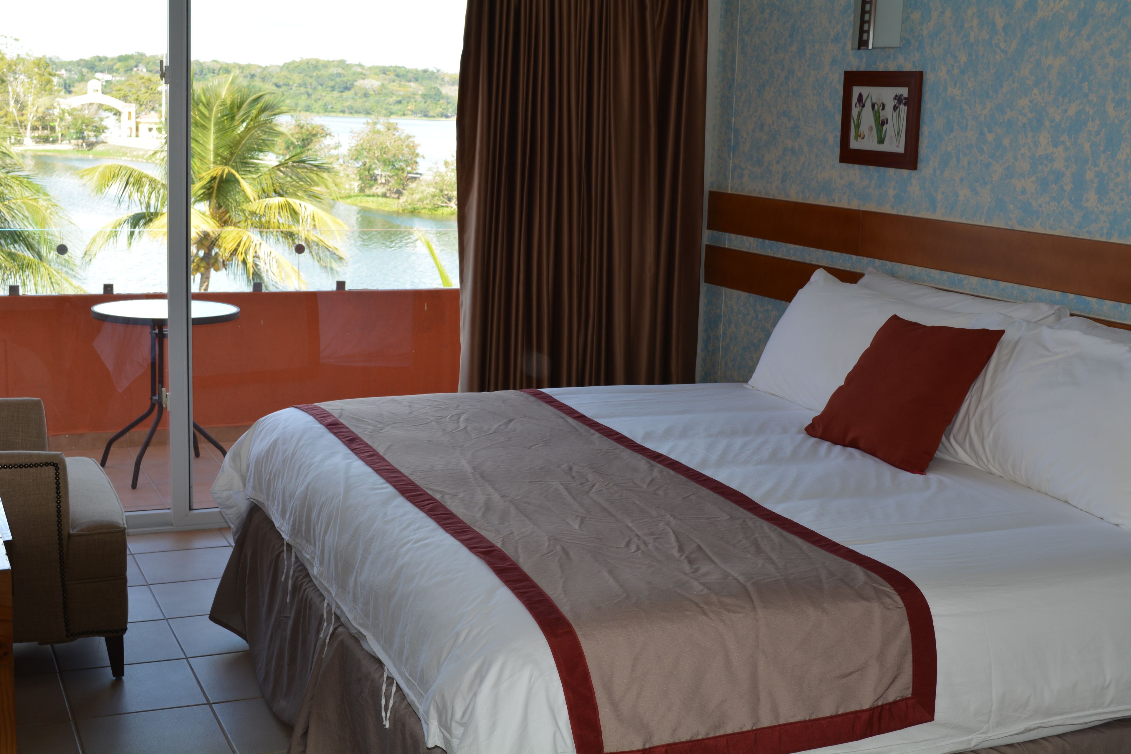 A hotel room with a large bed, a view of a lake, and a balcony with a chair.