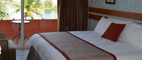A hotel room with a large bed, a view of a lake, and a balcony with a chair.
