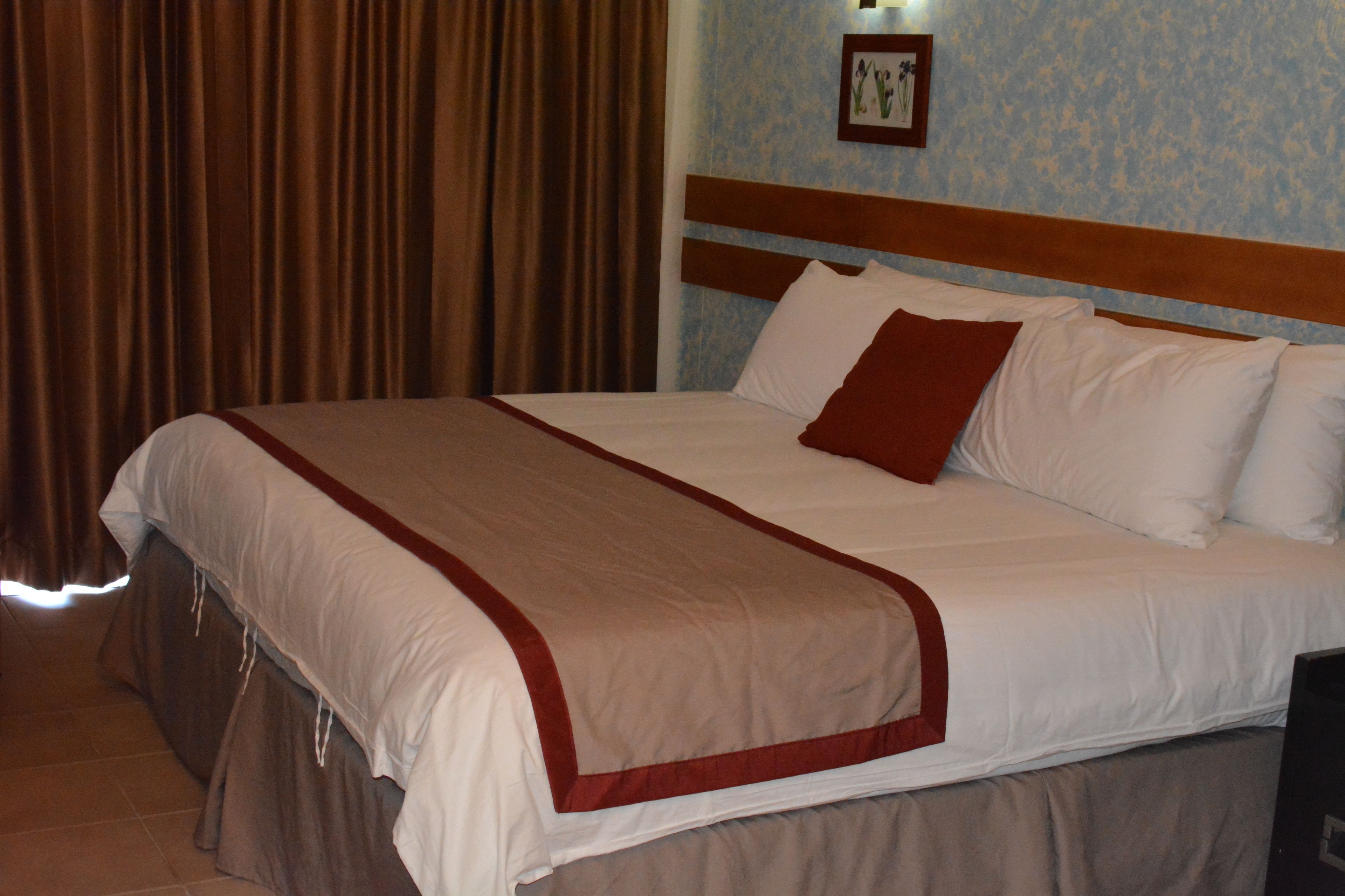 Una cama bien tendida con cabecera de madera, almohada decorativa roja y manta blanca.
