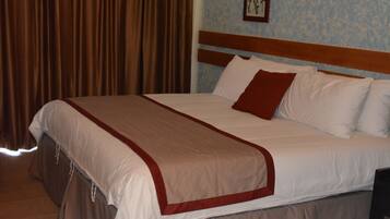 Una cama bien tendida con cabecera de madera, almohada decorativa roja y manta blanca.