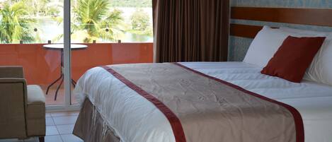 A hotel room with a bed, a chair, a view of a body of water, and a balcony.