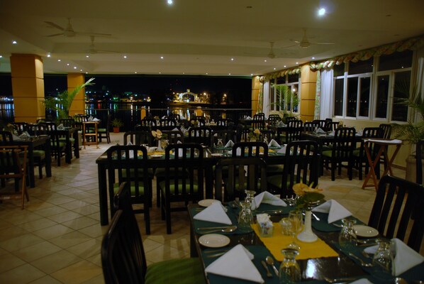 Un restaurante con varias mesas y sillas, piso de baldosas y vista a un edificio al fondo.