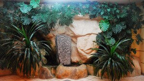 Une pièce dotée d’un sol carrelé, d’un mur en pierre orné de sculptures et de plantes tropicales.
