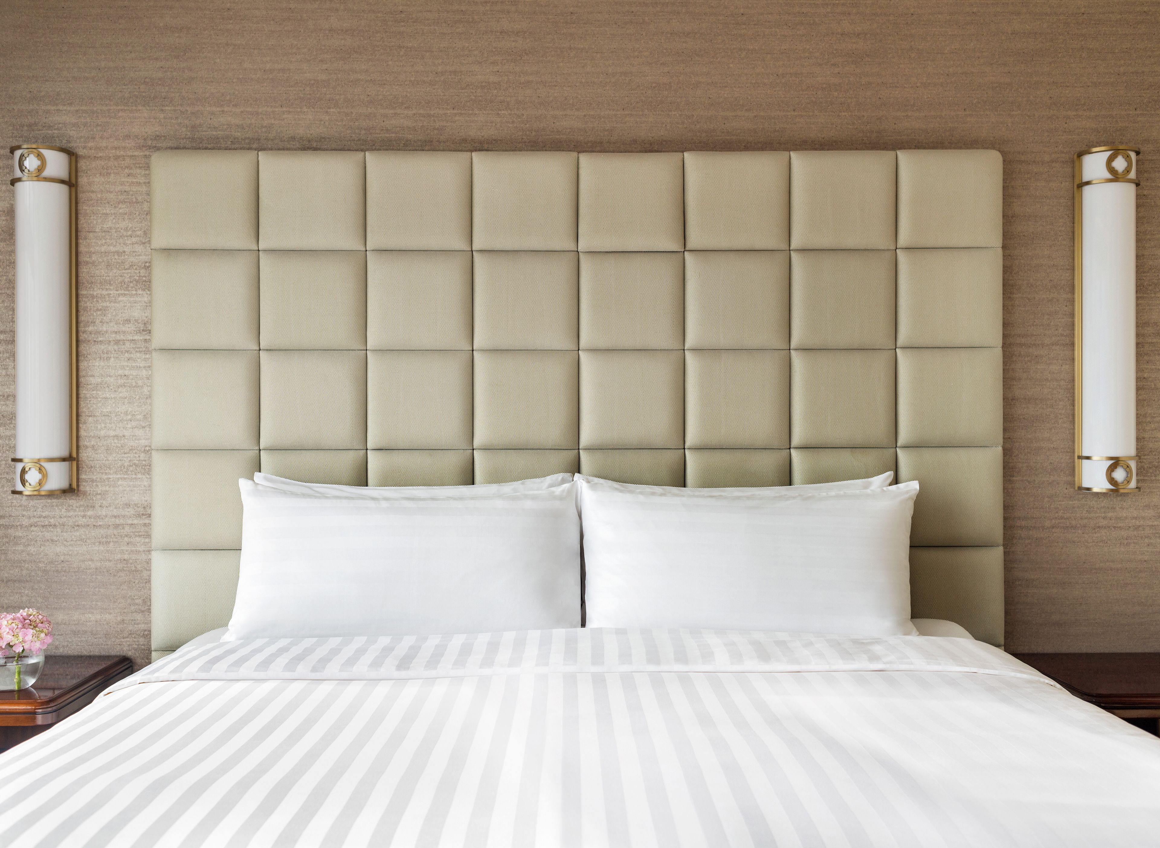 A neatly made bed with a tufted headboard, white bedding, and a vase of flowers on the nightstand.