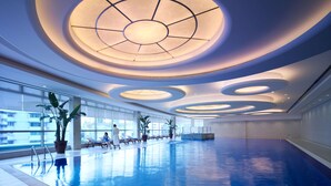 A modern indoor swimming pool with a skylight ceiling and lounge chairs along the poolside.