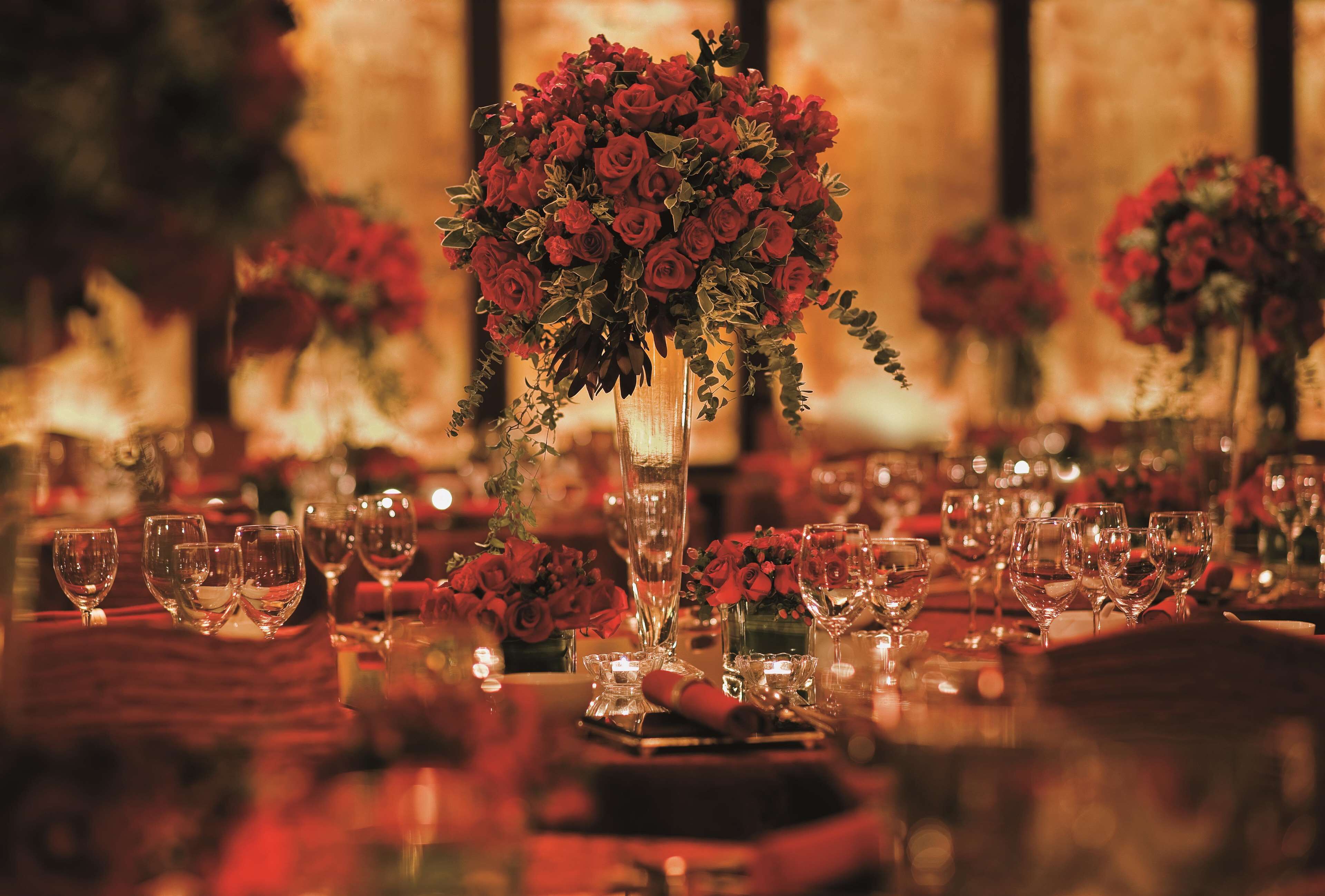 A table set with multiple wine glasses and a centerpiece of red roses in a tall vase.
