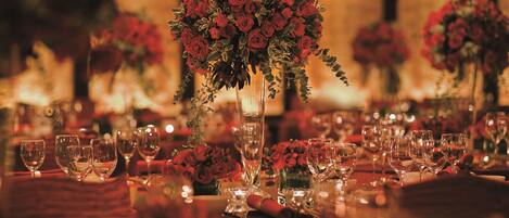 A table set with multiple wine glasses and a centerpiece of red roses in a tall vase.