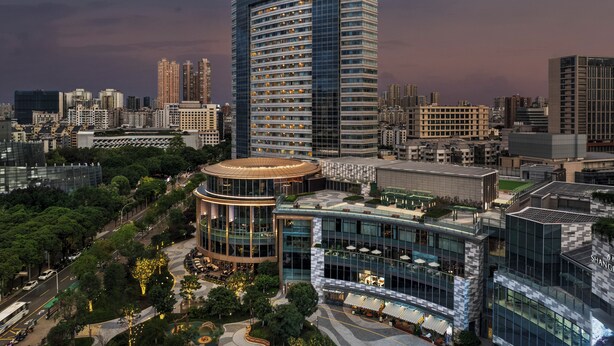 A modern hotel with a prominent curved glass facade, surrounded by urban buildings and greenery.