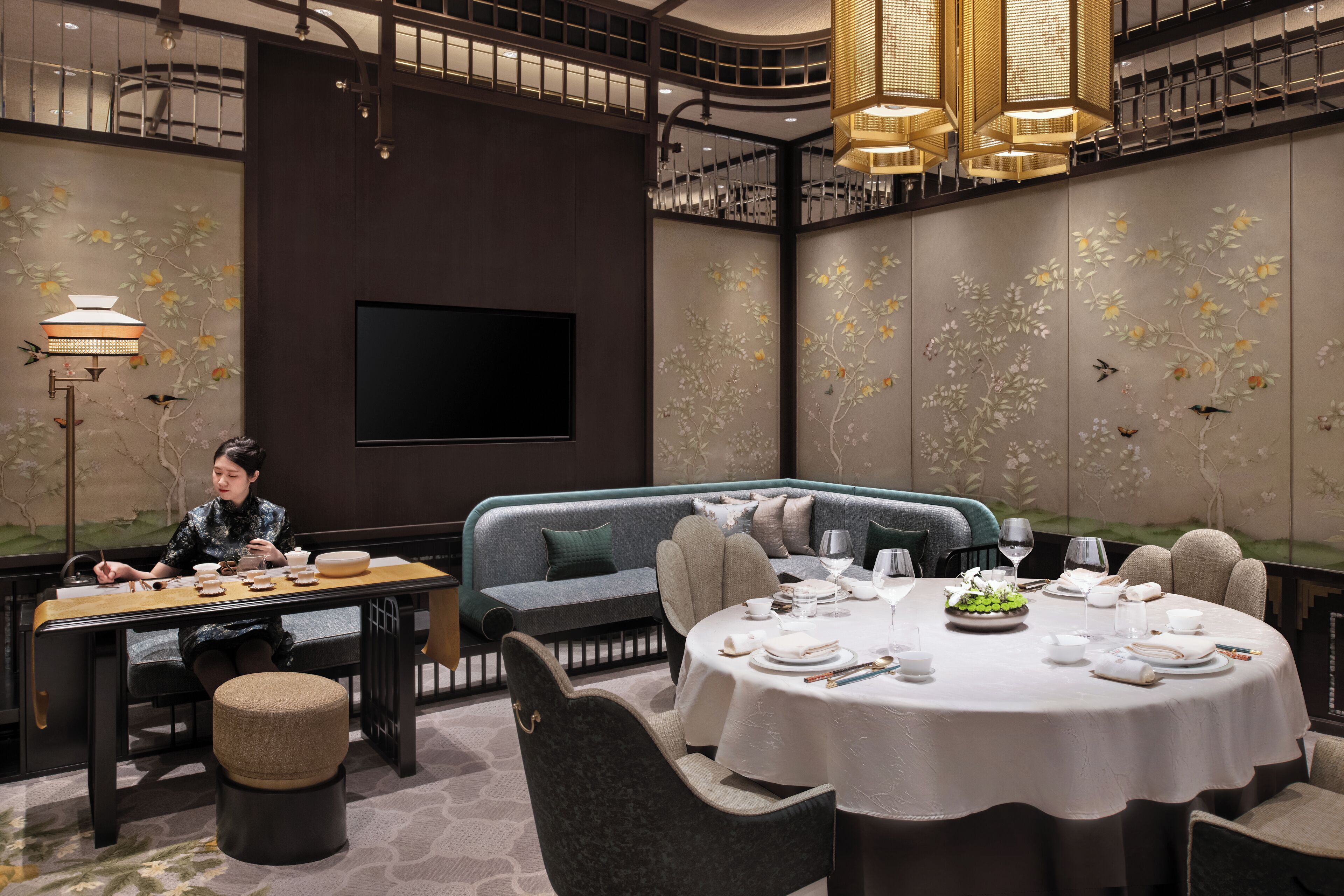 A dining area with a round table set for a meal, a sofa, and a television screen on the wall.