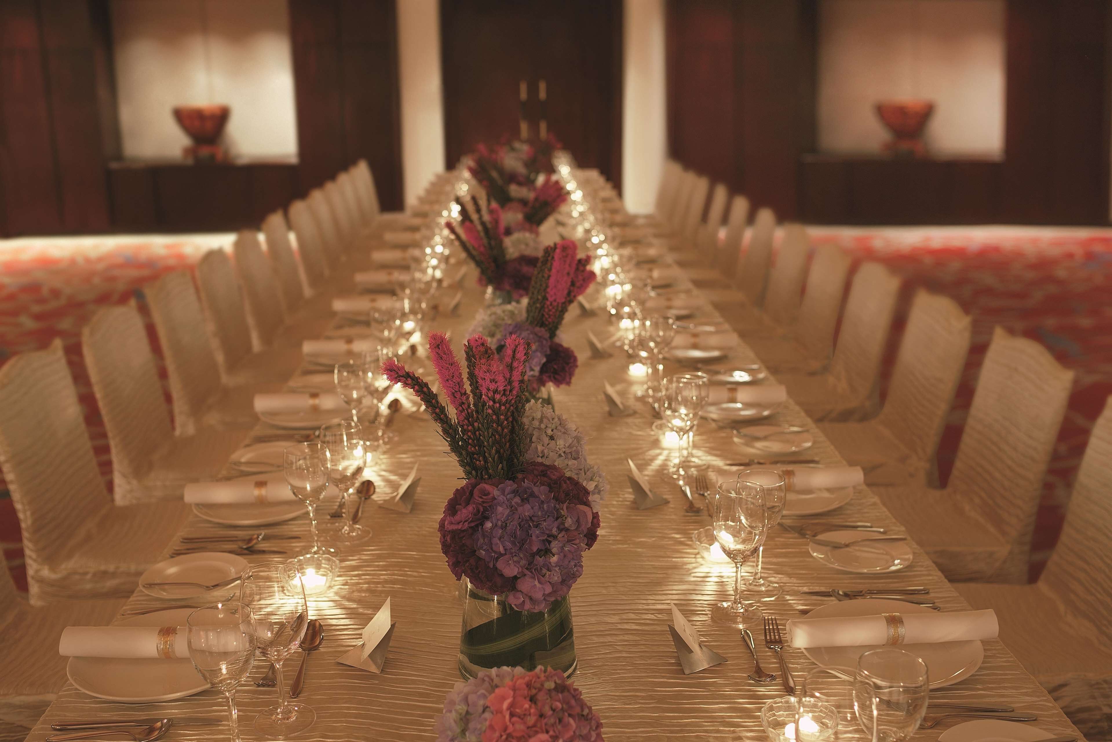 A long dining table set for a formal event with floral centerpieces, candles, and neatly arranged tableware.