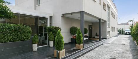 Um edifício moderno com fachada plana, grandes janelas e área de entrada coberta com plantas em vasos.