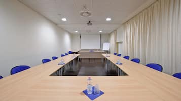 Un salón de conferencias con una larga mesa, sillas azules, una pizarra y una pantalla para proyector.