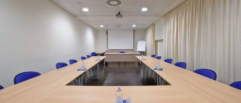 A conference room with a long table, blue chairs, a whiteboard, and a projector screen.