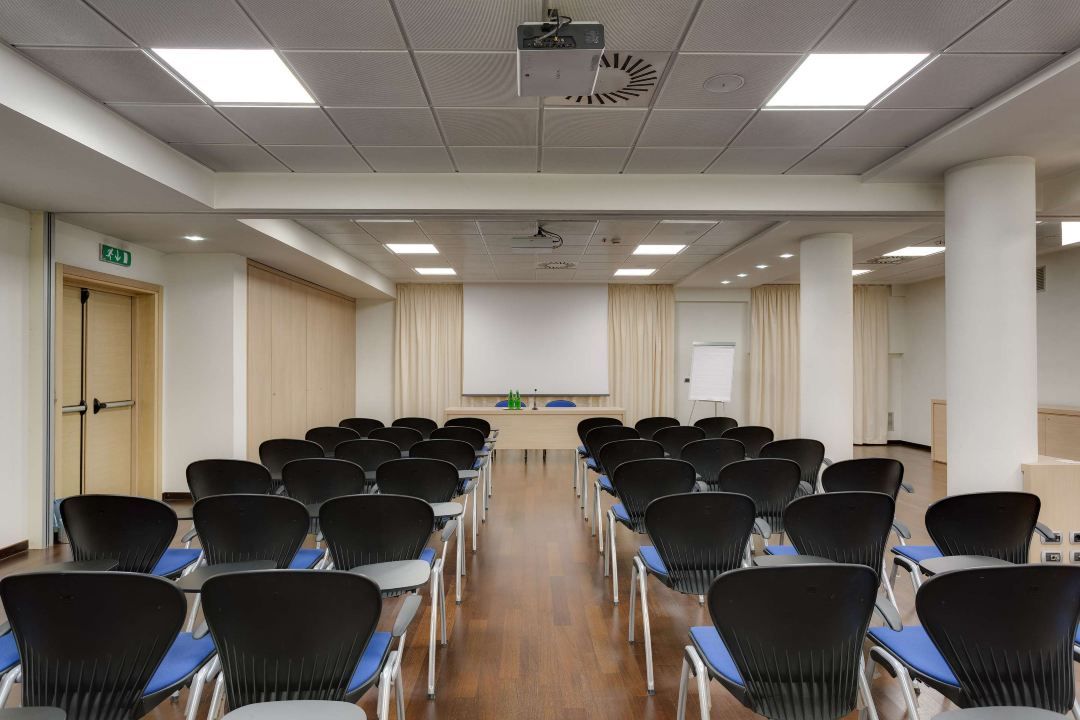 Ein Konferenzraum mit Reihen von Stühlen, einem Projektor, einer Tafel und einem Rednerpult.
