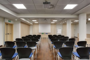 Una sala conferenze con file di sedie, un proiettore, una lavagna e un podio.