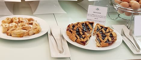 Una barra de buffet con diversos alimentos, incluyendo pasteles, una tarta y un bol de huevos.
