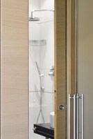 Un bagno moderno con box doccia in vetro, porta carta igienica a vista e stipite in legno.