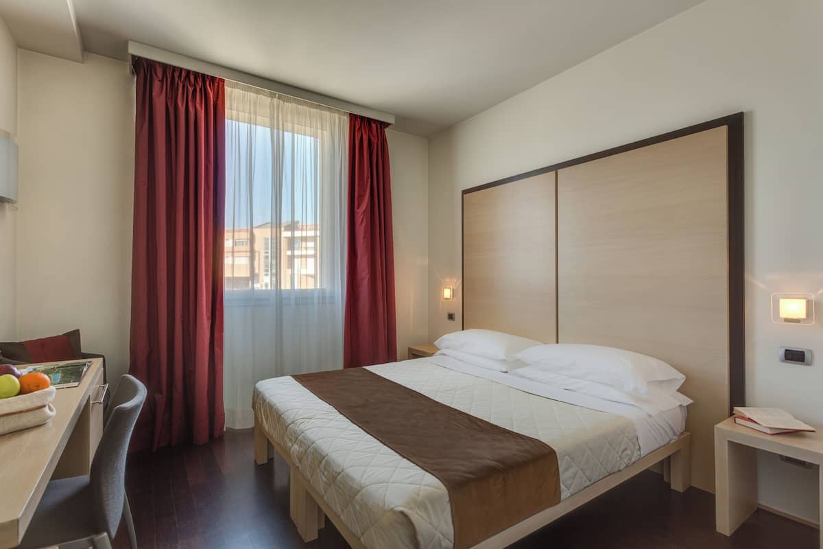 Een hotelkamer met een bed, nachtkastjes, een bureau en een stoel.