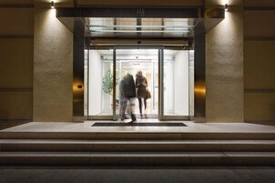 Ingresso di un hotel con porta in vetro, struttura in metallo e un lampadario.