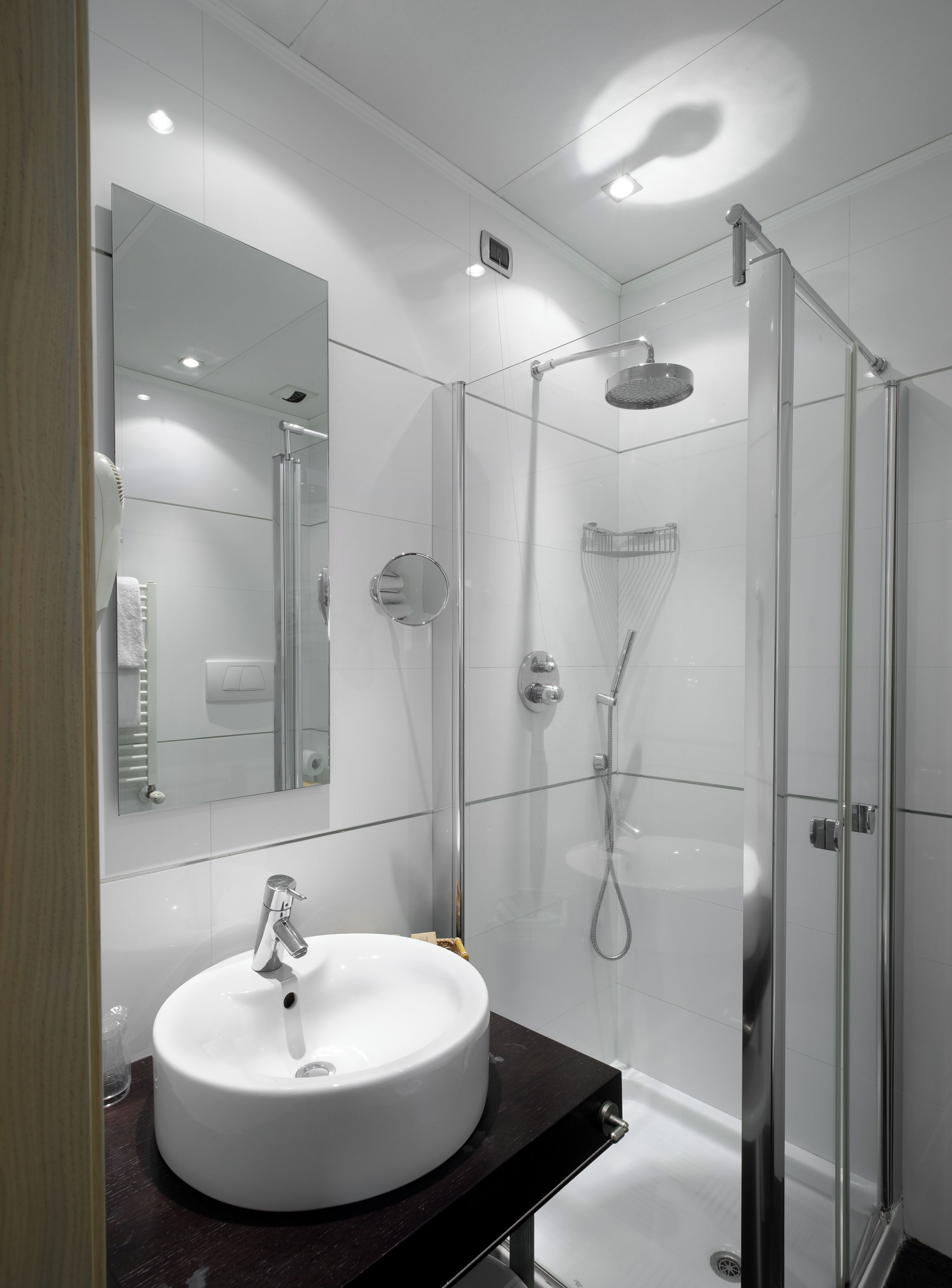 Un baño moderno con un lavabo redondo, una cabina de ducha de vidrio y un espejo grande.