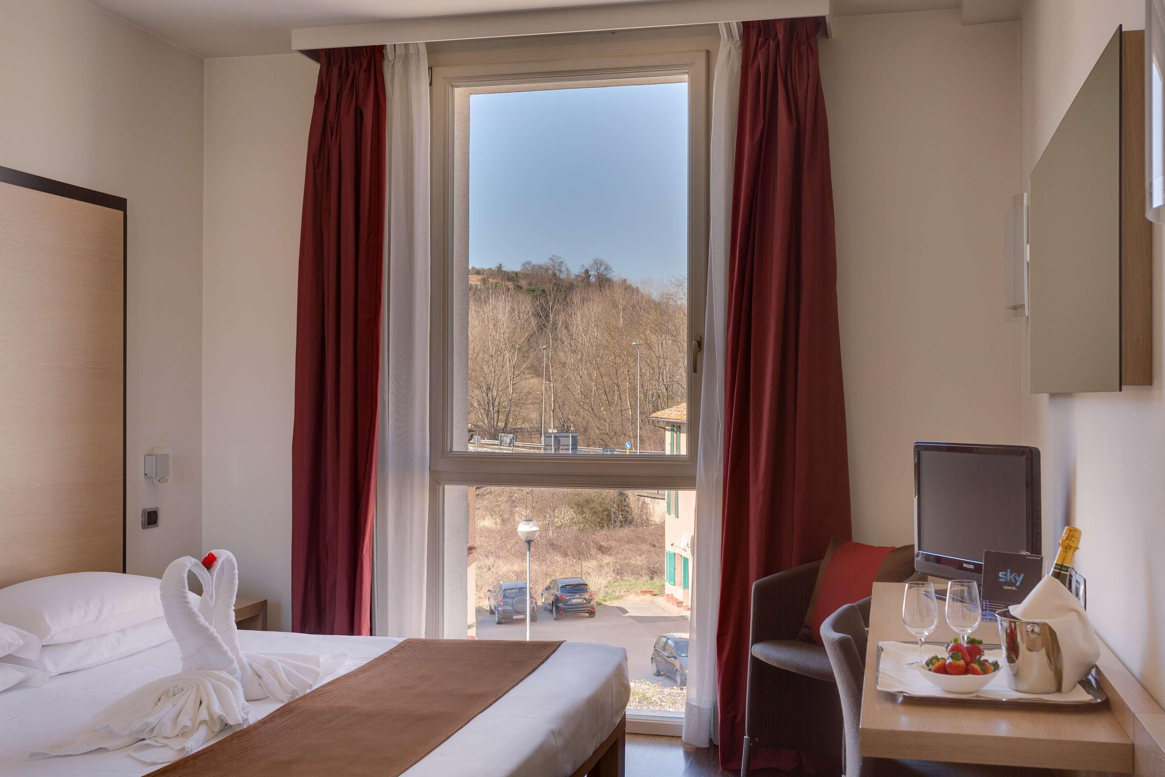 Ein Hotelzimmer mit Bett, Schreibtisch mit Computer, einer Champagnerflasche und Blick ins Freie.