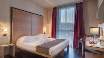 Ein Hotelzimmer mit einem Bett, Nachttischen, einem Schreibtisch mit Stuhl, einem Fernseher und einem Fenster mit Vorhängen.