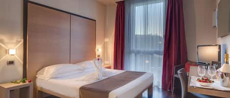Habitació d'hotel amb un llit, taules de nit, escriptori amb cadira, televisió i finestra amb cortines.