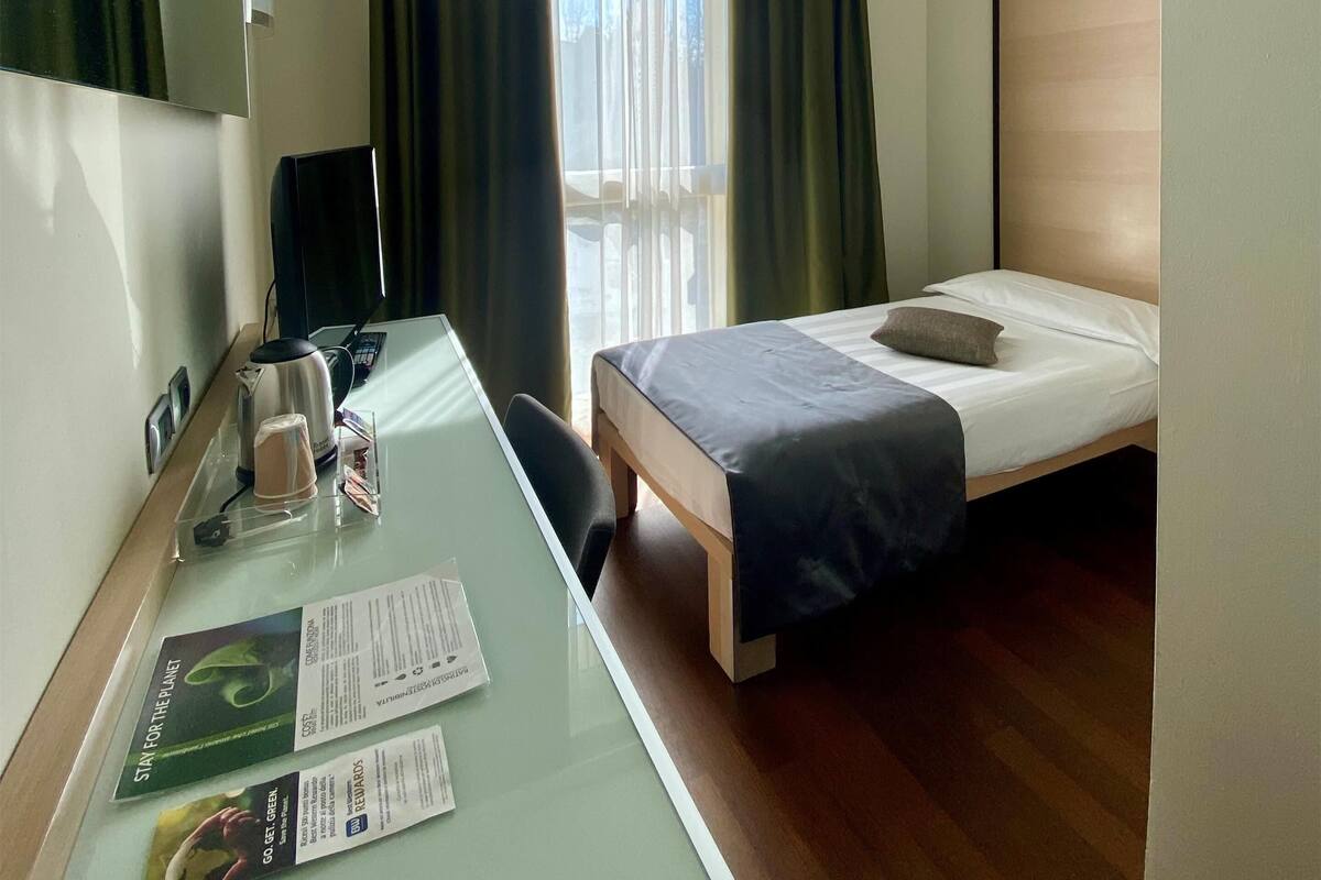 Een hotelkamer met een bed, een bureau met een computer, een waterkoker en een koffiekop.