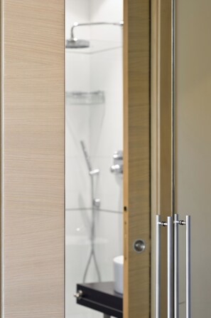 A modern bathroom with a glass shower enclosure, a visible toilet paper holder, and a wooden door frame. - Best Western Hotel San Marco (Siena)