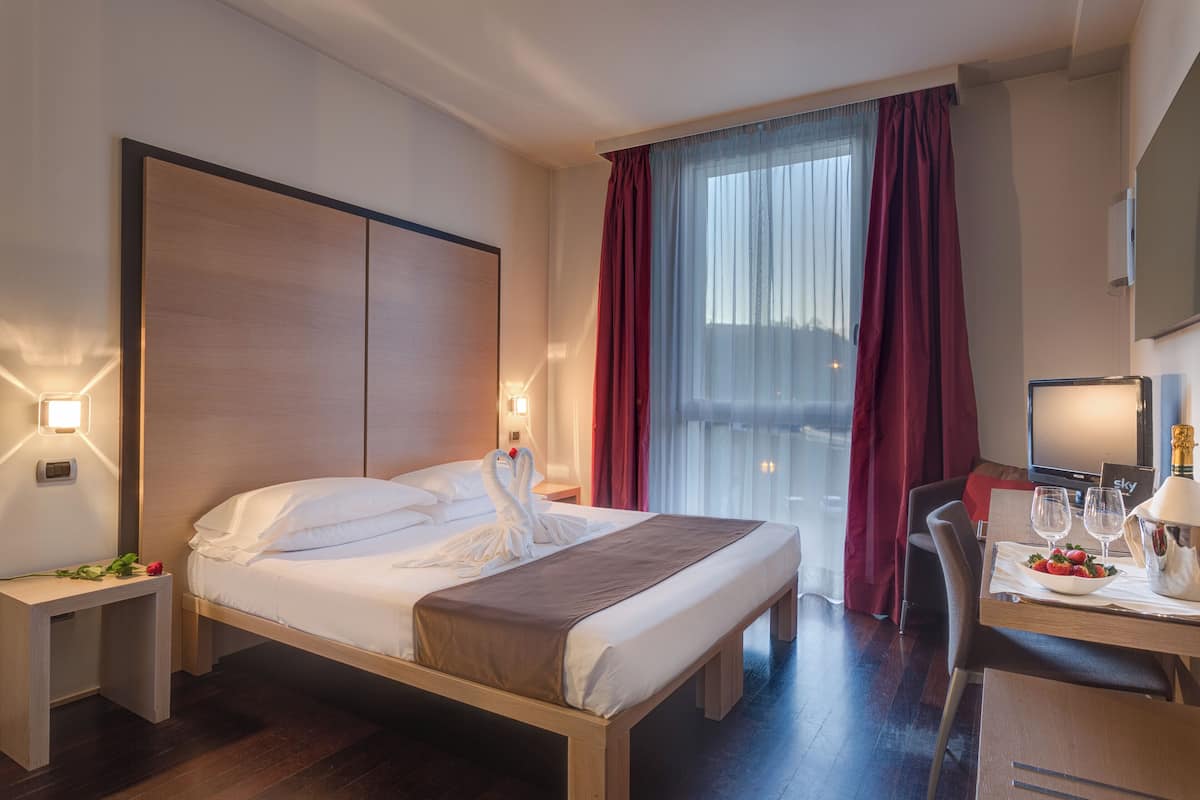 Een hotelkamer met een bed, nachtkastjes, een bureau met stoel, een televisie en een raam met gordijnen.