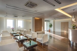 Un'area d'attesa moderna con sedie bianche, tavoli in vetro e una reception.