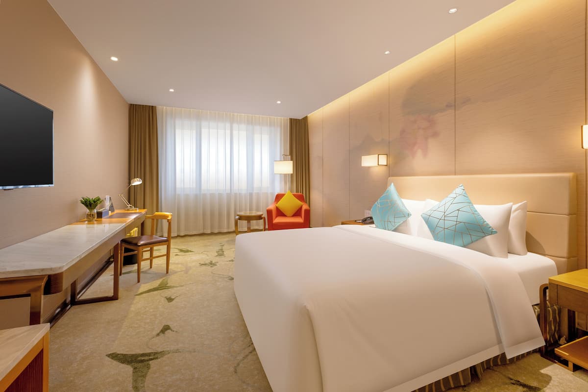 Een hotelkamer met een groot bed, een bureau, een stoel, een televisie en een raam met gordijnen.