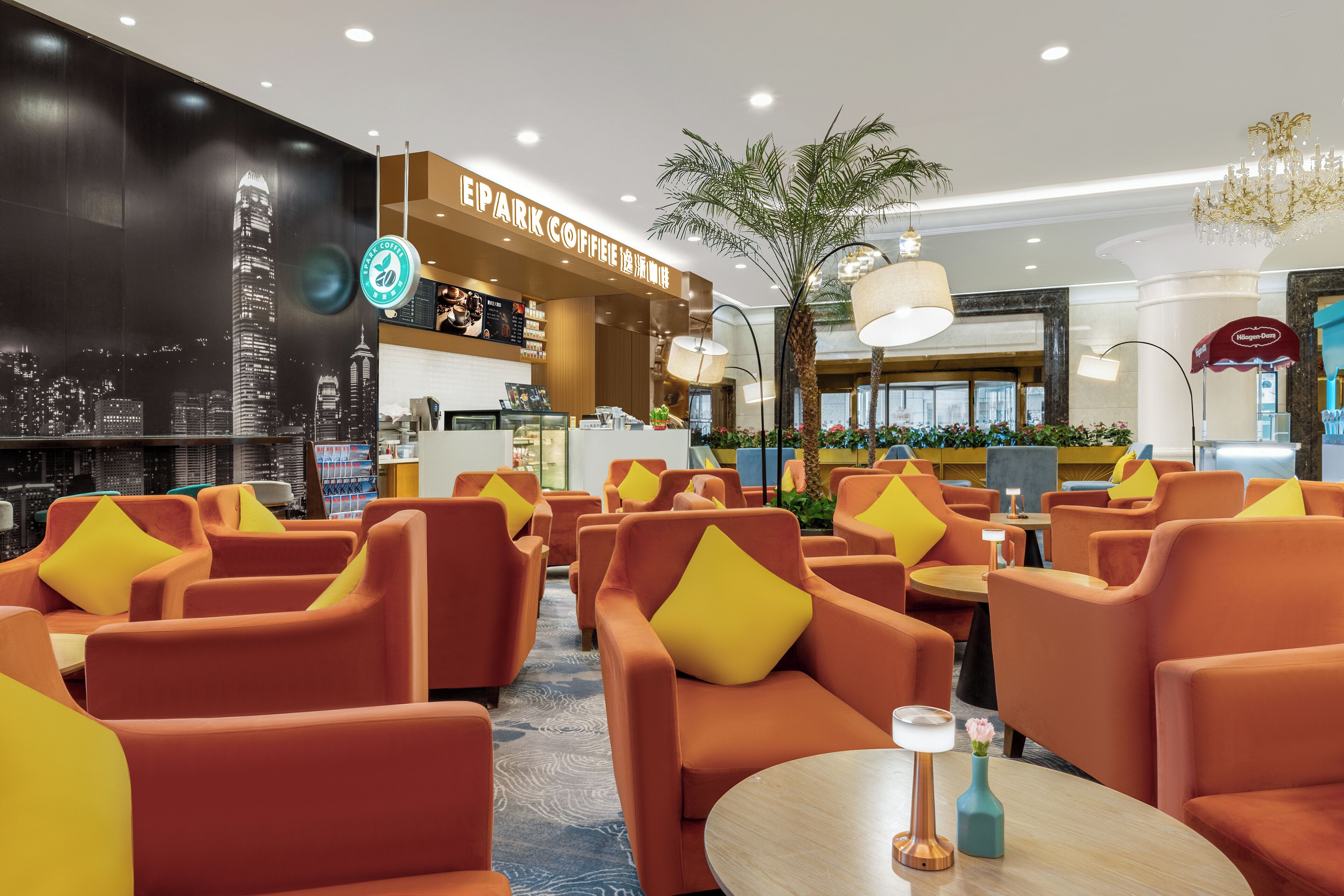 Et moderne loungeområde med orange siddepladser, en kaffebar og et bylandskabsmaleri.