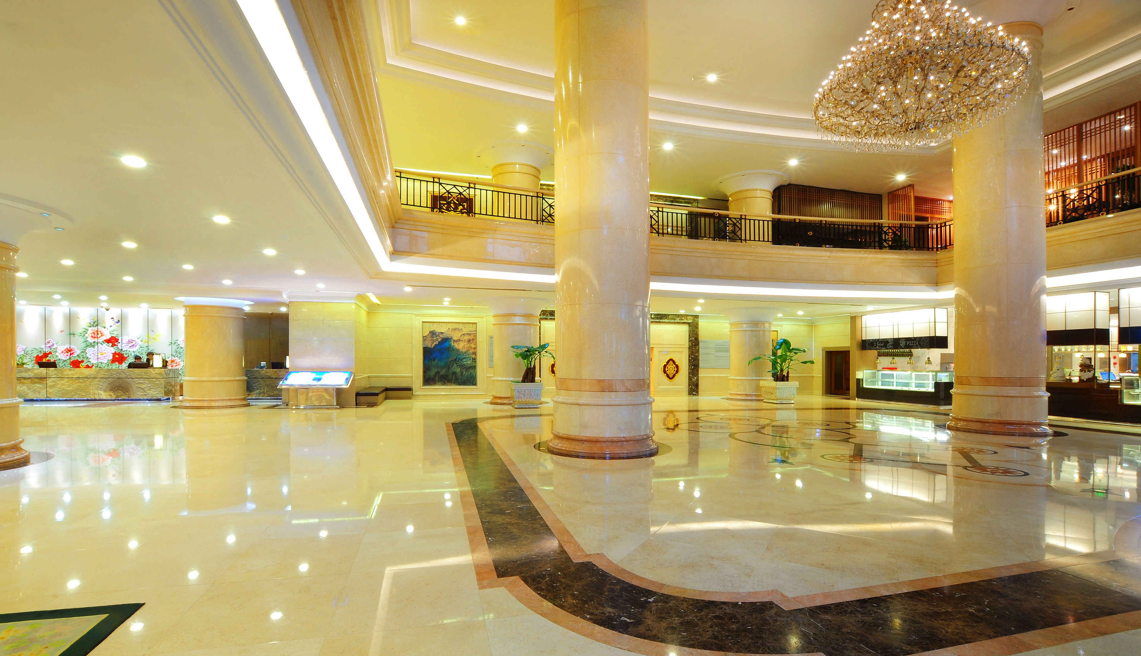 A spacious lobby with a high ceiling, marble flooring, and a central chandelier.