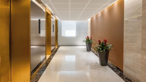 Un pasillo moderno con piso pulido, techo con diseño geométrico y dos plantas en macetas.