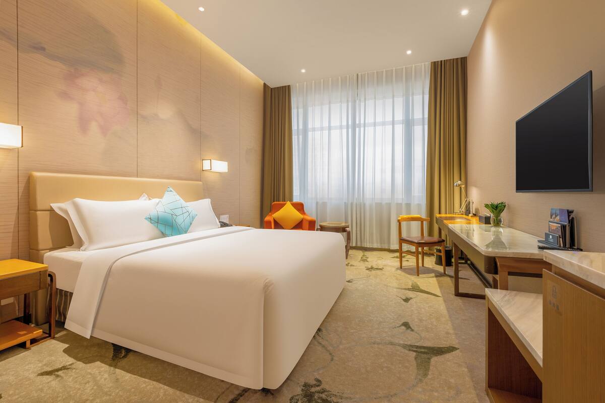 Een hotelkamer met een groot bed, een bureau, een stoel en een aan de muur bevestigde televisie.