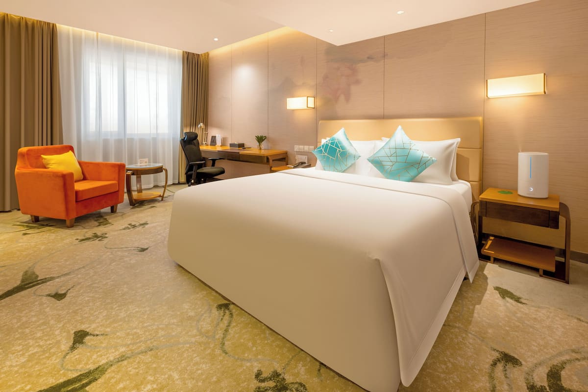 Een hotelkamer met een groot bed, een bureau, een stoel en een nachtkastje met een lamp.
