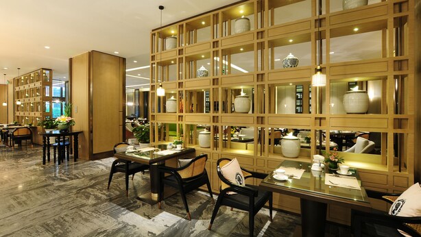 Un comedor moderno con un separador de madera, mesas, sillas y adornos.