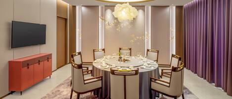Une salle à manger moderne avec une table ronde, six chaises, un téléviseur à écran plat et un buffet rouge.